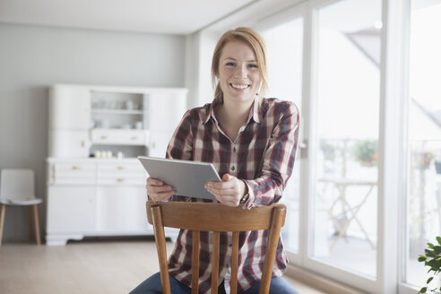 Porträt einer lächelnden jungen Frau mit ihrem digitalen Tablet zu Hause - RBF003851
