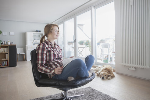 Junge Frau mit Zeitschrift entspannt auf einem Ledersessel zu Hause - RBF003855