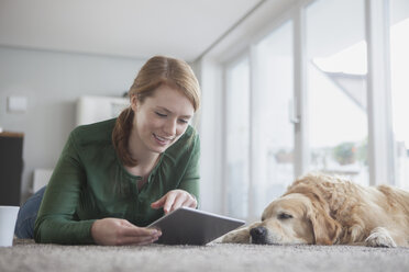 Smiling young woman lying beside her sleeping dog on the carpet using digital tablet - RBF003864