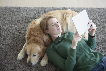 Smiling young woman lying with her dog on the carpet using digital tablet - RBF003867