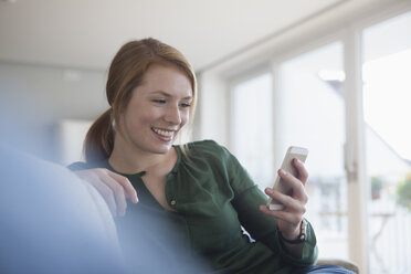 Portrait of smiling young woman on the couch looking at smartphone - RBF003876