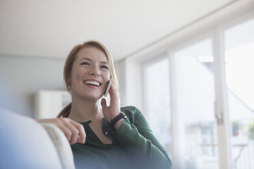 Porträt einer lächelnden jungen Frau auf der Couch, die mit einem Smartphone telefoniert - RBF003877