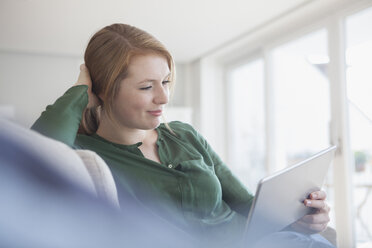 Portrait of smiling young woman with digital tablet relaxing on the couch - RBF003878