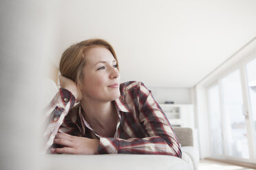 Lächelnde junge Frau entspannt sich auf der Couch - RBF003882