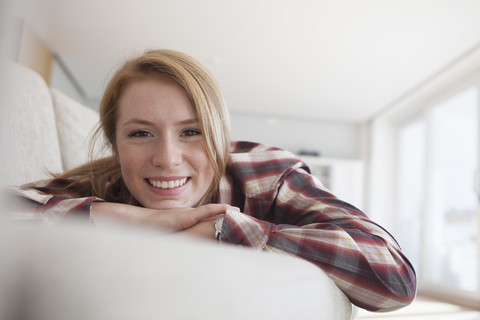 Porträt einer lächelnden jungen Frau, die sich auf der Couch entspannt, lizenzfreies Stockfoto