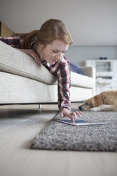 Lächelnde junge Frau, die ein digitales Tablet benutzt, während sie auf der Couch liegt - RBF003885