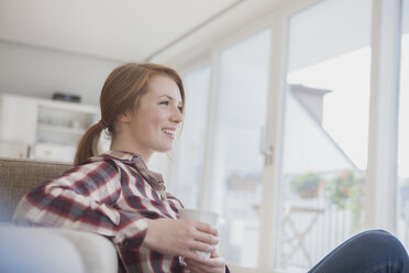 Smiling young woman relaxing with cup of coffee at home - RBF003888