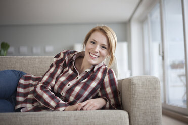 Porträt einer lächelnden jungen Frau, die zu Hause auf der Couch liegt - RBF003891