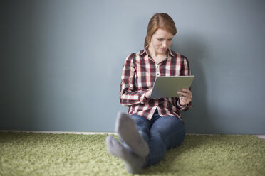 Smiling young woman sitting on the floor using digital tablet - RBF003892