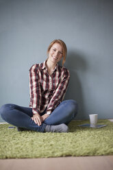 Portrait of smiling young woman sitting on the floor - RBF003895