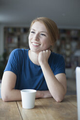 Portrait of smiling young woman sitting at table with cup of coffee - RBF003896