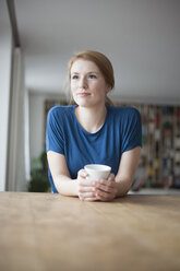 Porträt einer jungen Frau, die mit einer Tasse Kaffee am Tisch sitzt - RBF003897