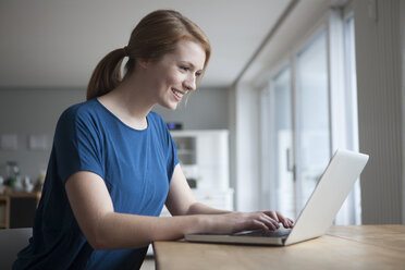 Lächelnde junge Frau, die am Tisch sitzt und einen Laptop benutzt - RBF003901