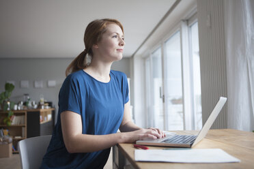 Young woman sitting at table with laptop - RBF003902