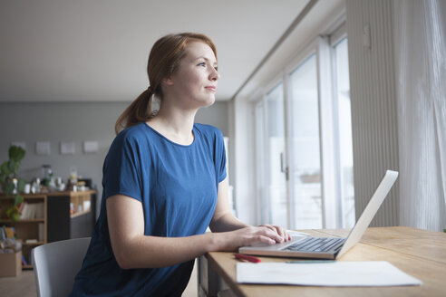 Junge Frau sitzt am Tisch mit Laptop - RBF003902