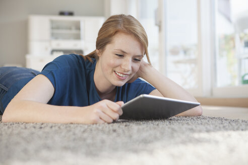 Porträt einer lächelnden jungen Frau mit digitalem Tablet, die sich zu Hause auf dem Boden entspannt - RBF003907