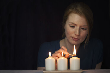 Porträt einer jungen Frau, die eine Kerze anzündet - RBF003909
