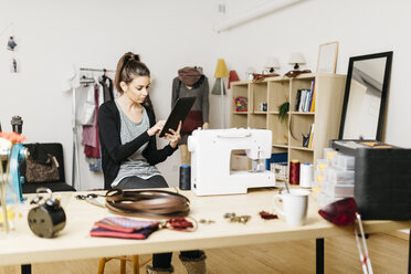 Young fashion designer working in her studio, using digital tablet - JRFF000278