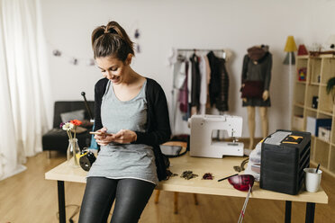 Junge Modedesignerin bei der Arbeit in ihrem Atelier, mit Smartphone - JRFF000280