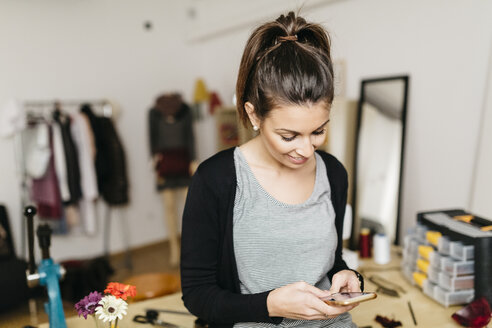 Junge Modedesignerin bei der Arbeit in ihrem Atelier, mit Smartphone - JRFF000281