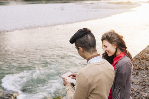 Italien, Belluno, junges Paar vor einem Fluss sitzend mit digitalem Tablet - ALBF000018