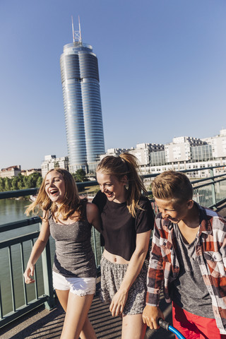 Österreich, Wien, drei glückliche Teenager, die auf einer Brücke vor dem Millenium Tower spazieren gehen, lizenzfreies Stockfoto