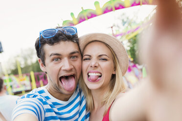 Glückliches Paar auf dem Jahrmarkt macht Selfie mit herausgestreckten Zungen - HAPF000100