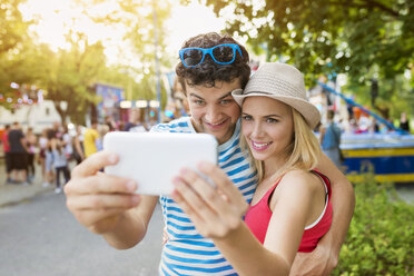 Glückliches Paar auf dem Jahrmarkt, das ein Smartphone-Selfie macht - HAPF000103