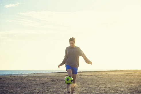 Spanien, Junge Frau spielt Fußball am Strand - KIJF000079