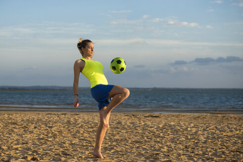 Spanien, Junge Frau spielt Fußball am Strand - KIJF000082