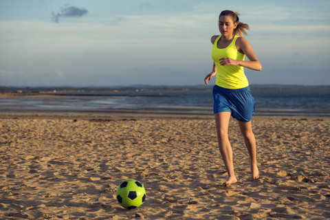 Spanien, Junge Frau spielt Fußball am Strand, lizenzfreies Stockfoto