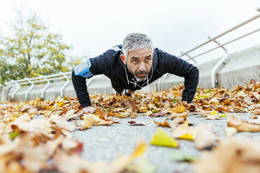 Mann macht Liegestütze, umgeben von Herbstblättern - AIF000162