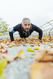 Mann macht Liegestütze, umgeben von Herbstblättern - AIF000163