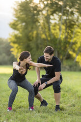 Man looking at woman doing knee bends in field - SHKF000414