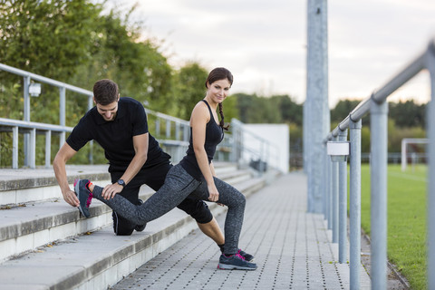 Mann hilft Frau beim Training auf dem Sportplatz, lizenzfreies Stockfoto