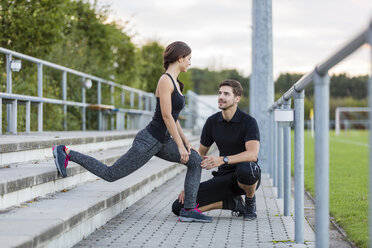 Man looking at woman exercising on sports field - SHKF000419