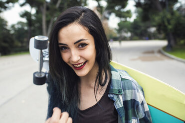 Portrait of smiling young woman with longboard behind her back - KIJF000092