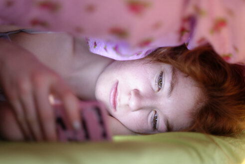 Porträt eines Mädchens, das unter einer Decke im Bett liegt und auf ihr Smartphone schaut - LBF001335