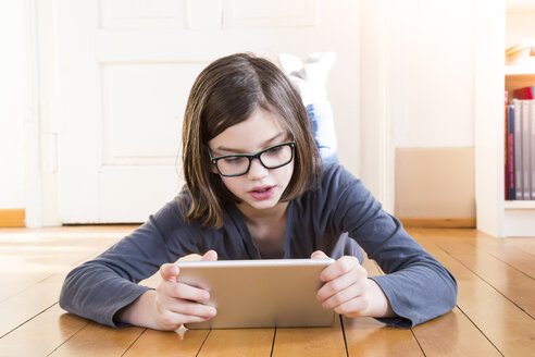 Porträt eines Mädchens, das auf einem Holzboden liegt und ein digitales Tablet benutzt - LVF004375
