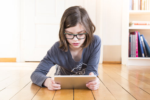 Porträt eines Mädchens, das auf einem Holzboden liegt und ein digitales Tablet benutzt - LVF004376