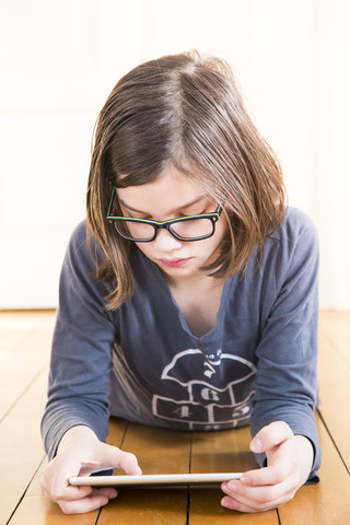 Porträt eines Mädchens, das auf einem Holzboden liegt und ein digitales Tablet benutzt, lizenzfreies Stockfoto