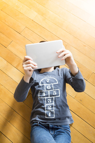 Girl lying on wooden floor covering her face with digital tablet stock photo