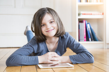 Porträt eines lächelnden Mädchens, das mit einem digitalen Tablet auf dem Holzboden liegt - LVF004380