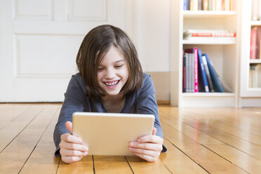 Porträt eines Mädchens, das auf einem Holzboden liegt und ein digitales Tablet benutzt - LVF004381