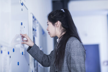 Chinese woman looking at information on pinboard - SGF001982