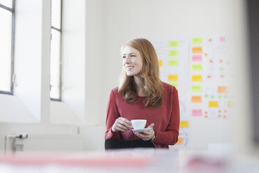 Junge Frau im Büro trinkt Kaffee - RBF003925