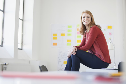 Junge Frau im Büro sitzt am Schreibtisch und denkt nach, lizenzfreies Stockfoto