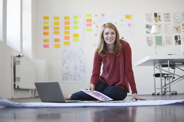 Young woman in office sitting on floor working through papers - RBF003936