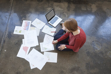 Junge Frau im Büro sitzt auf dem Boden und arbeitet Papiere durch - RBF003937