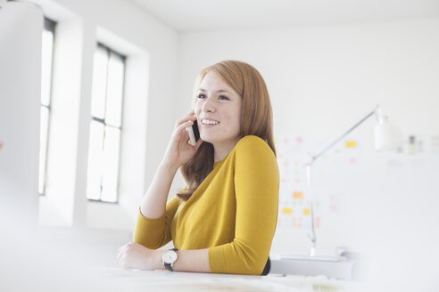 Junge Frau im Büro, die am Schreibtisch arbeitet und ein Smartphone benutzt - RBF003940